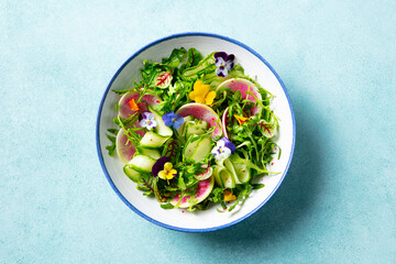 Green salad with watermelon radish and edible flowers in a bowl. Blue background. Close up. Top view.