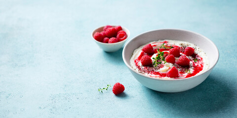Rice pudding dessert with berry sauce and fresh raspberries in a bowl. Blue background. Copy space.