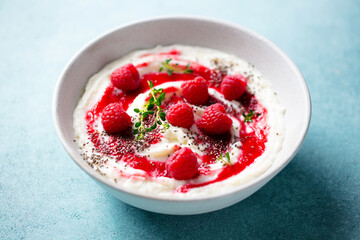 Rice pudding dessert with berry sauce and fresh raspberries in a bowl. Blue background. Close up.
