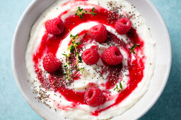 Rice pudding dessert with berry sauce and fresh raspberries in a bowl. Blue background. Close up.