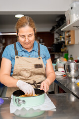 Pastry chef placing biscuit base in cake mold, preparing dessert in professional kitchen