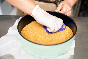 Pastry chef pressing cookie crumbs into baking pan for dessert crust