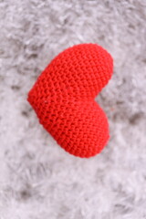 A small red knitted heart sits atop a pile of white fur, symbolizing warmth and love.