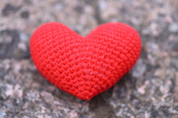 Fototapeta premium A small, vibrant red heart made of crochet sits atop a natural rock surface.