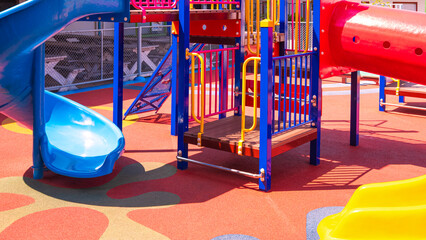 Colorful slides with playground equipment on rubber floor in outdoors playground area at kindergarten