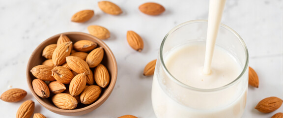 Creamy almond milk poured into a glass with whole almonds, dairy-free concept