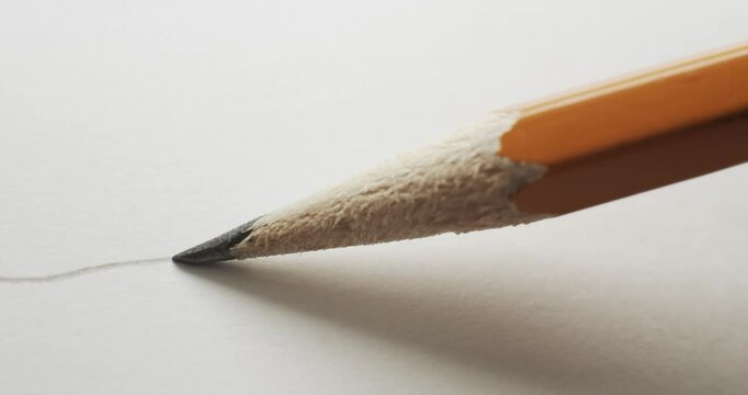 Yellow pencil with close up on sharp graphite pencil tip drawing a simple curvy line on plain white paper. Starting a pencil sketch with focus following the sharp lead writing a wavy doodle on paper.