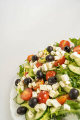 Fresh healthy vegetable Mediterranean salad of feta cheese, cucumber, tomato, olives, and green salad leaves, banner, close-up
