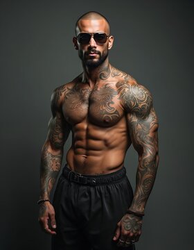 Studio portrait of muscular bearded bald man. Brutal male torso, tattoos on body. Strong fit muscles, abs, biceps, athletic body. Sunglasses. Sport lifestyle. Health, brutal force, potency.