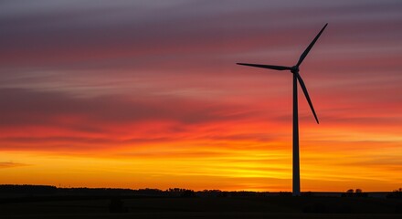 Obraz premium Wind turbine silhouette against a vibrant sunset sky showcasing hues of orange, purple, and pink symbolizing renewable energy and sustainability