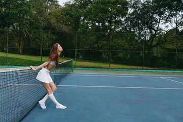 Obraz premium Energetic young woman in white tennis outfit joyful on outdoor court emphasizing healthy lifestyle and sports enthusiasm