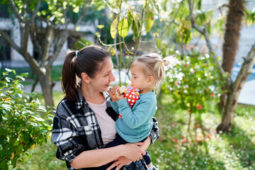 Obraz premium Smiling mother looking at little daughter sitting in her arms while standing in the garden