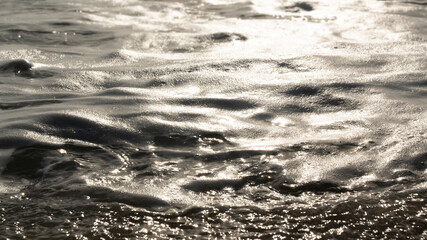 Sea water waves with reflection on golden sunset background.