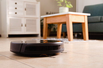 A black robot vacuum cleaner cleaning the floor at home. 