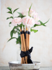 Calligraphy brushes tied with black ribbon in ceramic bowl with flowers in background