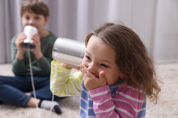 Boy and girl talking on tin can telephone indoors, selective focus