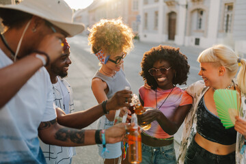 Happy friends toasting with beer bottles at sunset in the city
