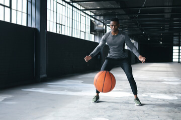 Athletic man practicing basketball dribbling skills in spacious warehouse setting, copy space