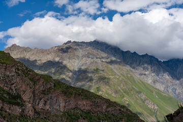 Fototapeta premium Rugged mountainous landscape with rocky peaks, lush green slopes, and scattered clouds casting shadows. A serene natural scene, ideal for nature, exploration, and outdoor themes.
