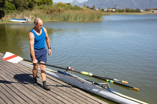 Senior man preparing rowing boat on lake dock, enjoying outdoor activity, copy space
