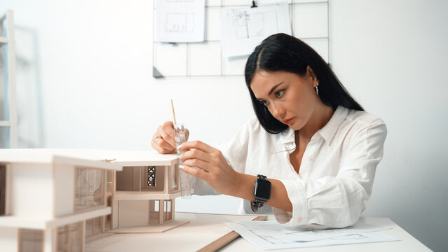 Closeup portrait image of professional young beautiful engineer architect using triangular scale measures house model with focusing at modern office. Business creative design concept. Immaculate.