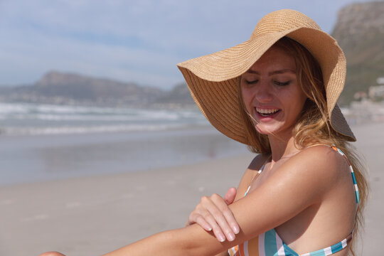 Smiling woman in sun hat enjoying morning beach sun, applying sunscreen, copy space - Powered by Adobe