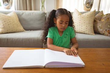 Young girl in green shirt reading large book at home, concentrating deeply, copy space