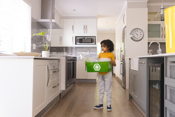 In kitchen, child holding recycling bin, learning about environmental responsibility, copy space