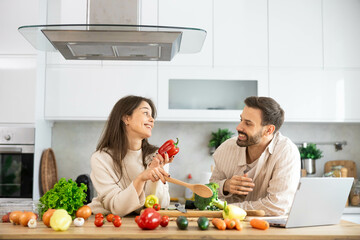 A joyful couple in the kitchen preparing a meal together with vibrant vegetables, highlighting love for cooking and nutrition.