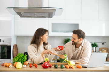 A couple sharing laughter in the kitchen, surrounded by fresh vegetables, embodying joy and love for their culinary journey.
