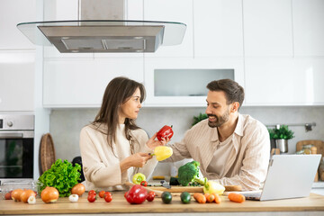 A loving couple shares a joyful cooking experience in the kitchen surrounded by fresh vegetables and positive vibes of togetherness.