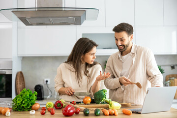 The couple shows curiosity and interest while pondering over a recipe, surrounded by fresh vegetables in the kitchen.