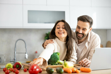 A playful couple enjoys cooking together, surrounded by an array of colorful vegetables in a stylish kitchen setting.