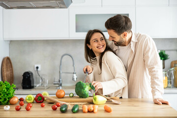 A joyful couple chops broccoli in their modern kitchen, filled with fresh produce, embodying healthy living and togetherness.