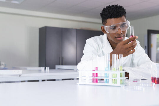 Teenager in school laboratory examining test tube with focused expression, copy space