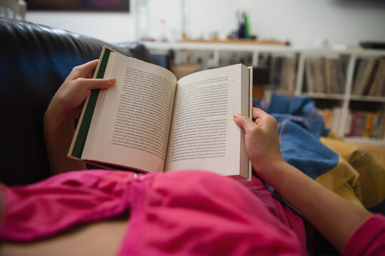 Relaxing at home, person reading book on couch, enjoying leisure time