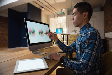 Focused Asian man designing on computer in modern office with digital tablet, copy space