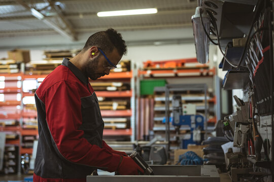 Factory worker in protective gear inspecting tools in busy industrial workshop, copy space