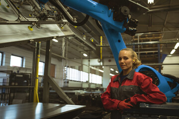 In factory, engineer in red uniform standing confidently beside industrial machinery, copy space