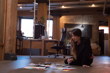 Creative Asian woman brainstorming ideas on floor with colorful papers in office, copy space