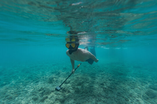 Man snorkeling underwater with action camera exploring coral reef in clear ocean