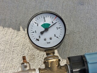 A close-up of a pressure gauge showing the level on white dial with its metal pipe connections.