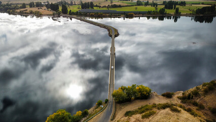 A long bridge over a shallow and calm dark lake on a cloudy day, seen from above
