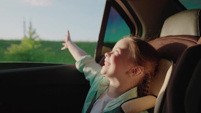 Happy child enjoying car ride, girl smiling backseat, kid feeling wind through the window, road trip with family, joyful childhood moment, excited young traveler, summer adventure road, cheerful