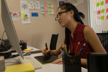 Asian woman using digital tablet and computer at office, focused on design work, copy space