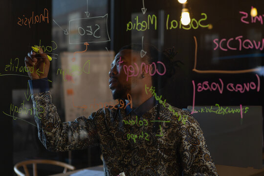 Businessman writing marketing strategy on glass board in modern office, copy space