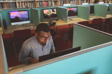 In library, focused man using computer in study cubicle, concentrating on work, copy space