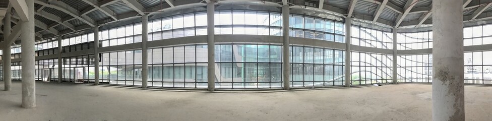 The interior of a building under construction features concrete pillars and large window views.