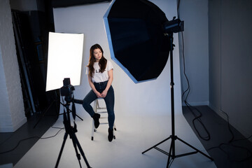 Young woman sitting on stool in photography studio with professional lighting