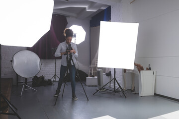 African American woman adjusting camera on tripod in professional photography studio, copy space
